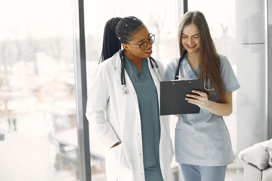 Two healthcare professionals review a patient's care plan together beside a bright window.