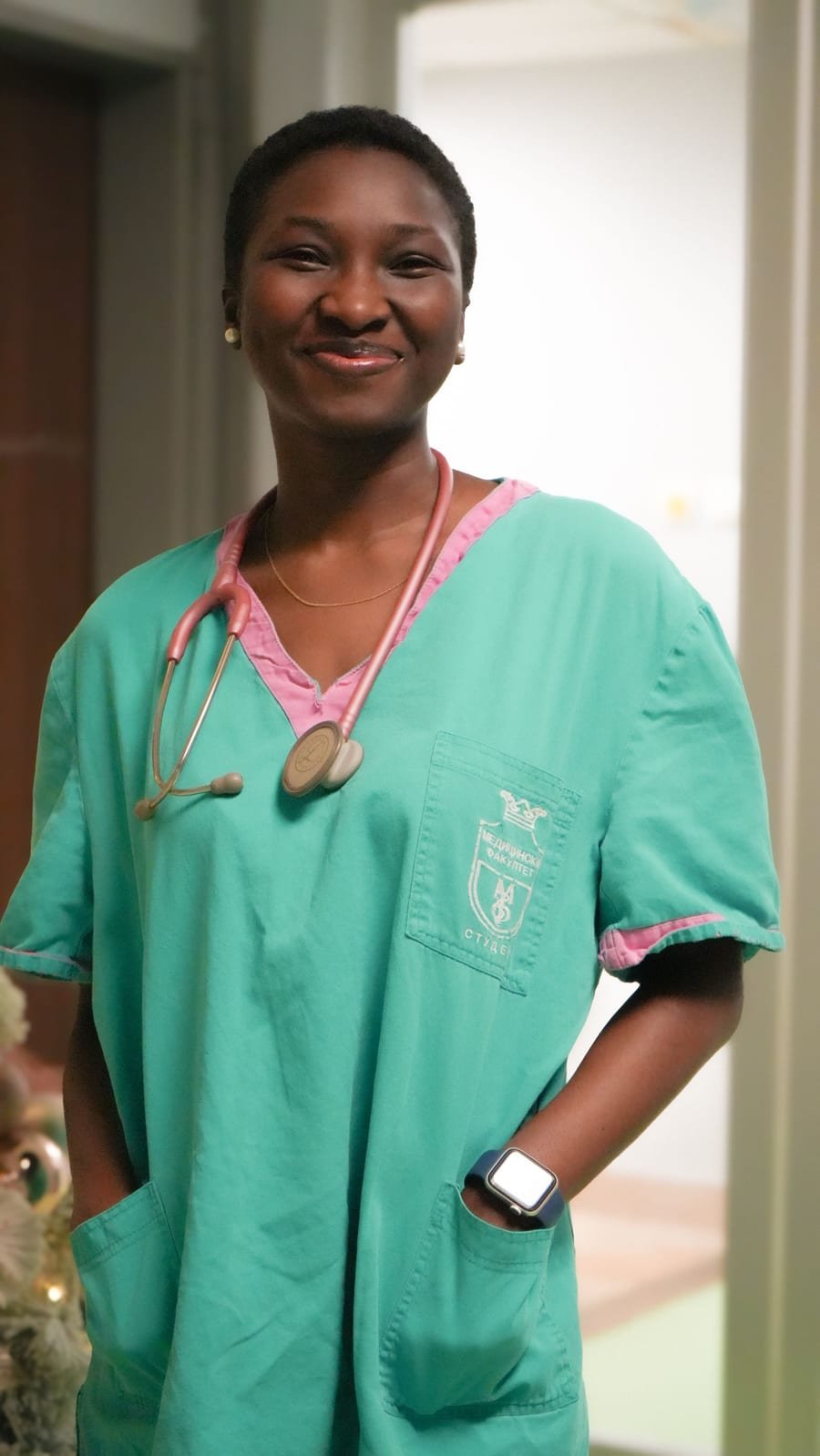 A home health nurse in scrubs smiles warmly, ready for a home visit.