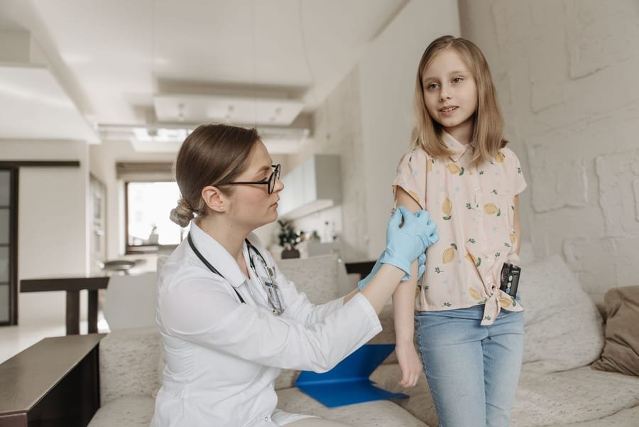 A nurse checks a smiling child's arm during a relaxed home visit.